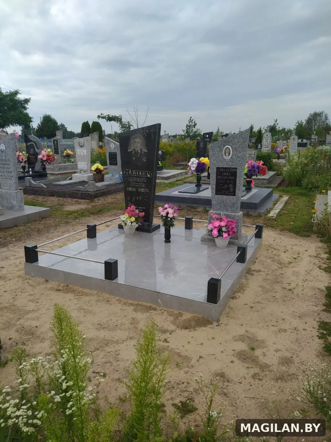 Два памятника на общей тёмной плиточной площадке с металлическими ригелями в Ляховичском районе