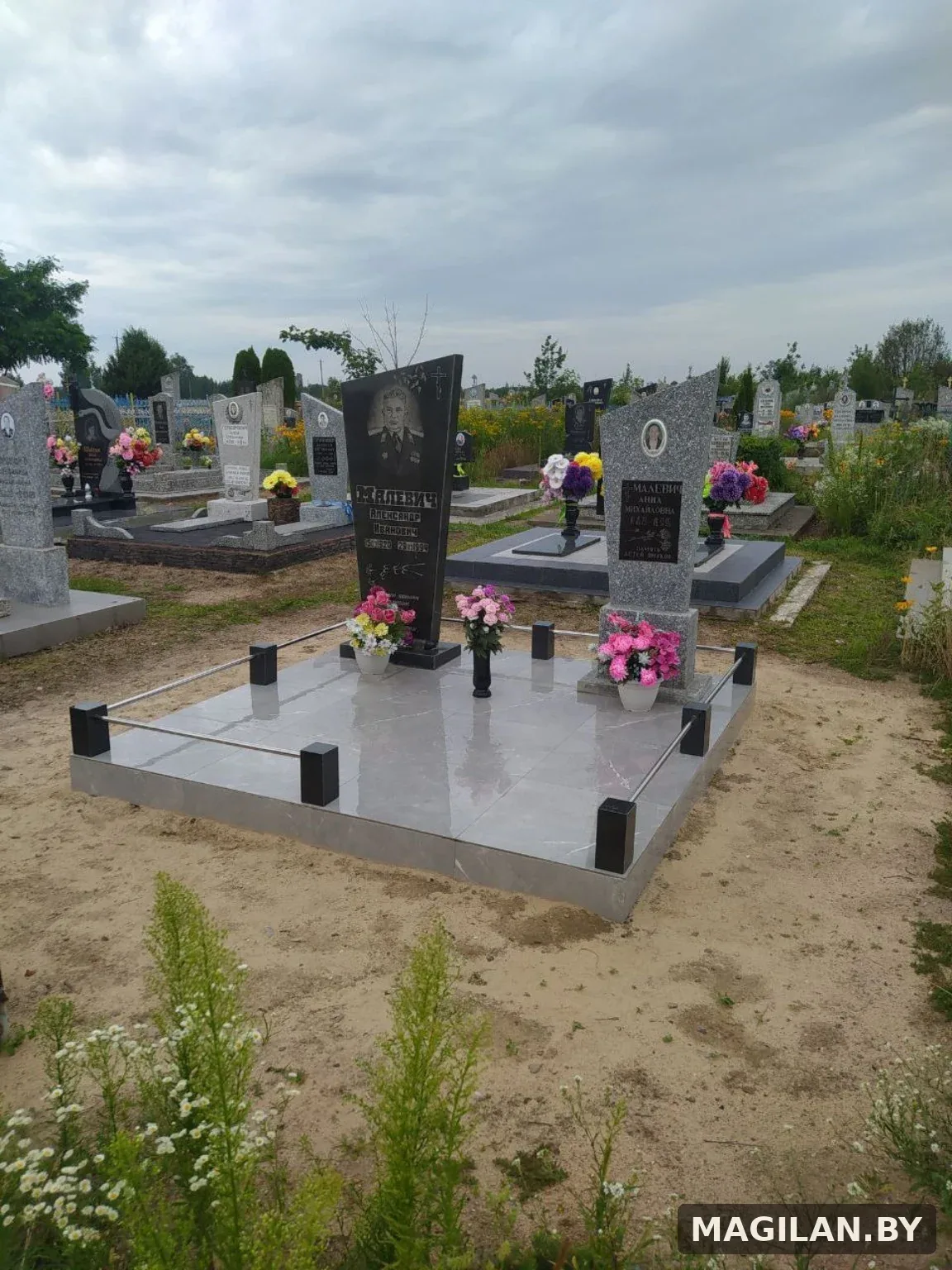Два памятника на общей тёмной плиточной площадке с металлическими ригелями в Ляховичском районе